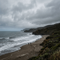 Foggy coastal beach with ocean waves, cliffs, and people walking on sand